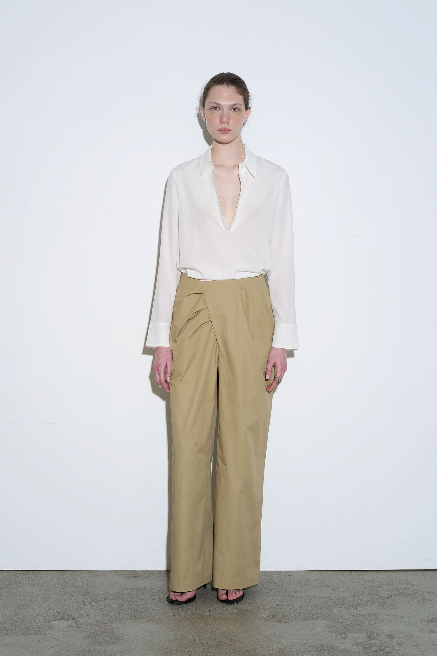 The Loom beige asymmetrical wrap trousers front view with pleated detail and wide leg silhouette