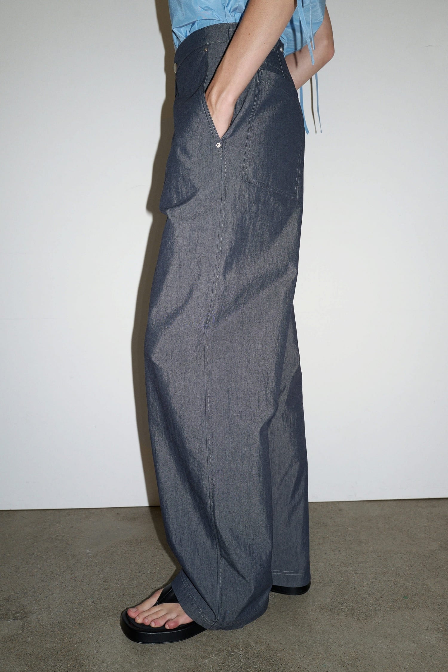 Side view of The Loom indigo denim barrel trousers showing curved leg silhouette and front pocket detail