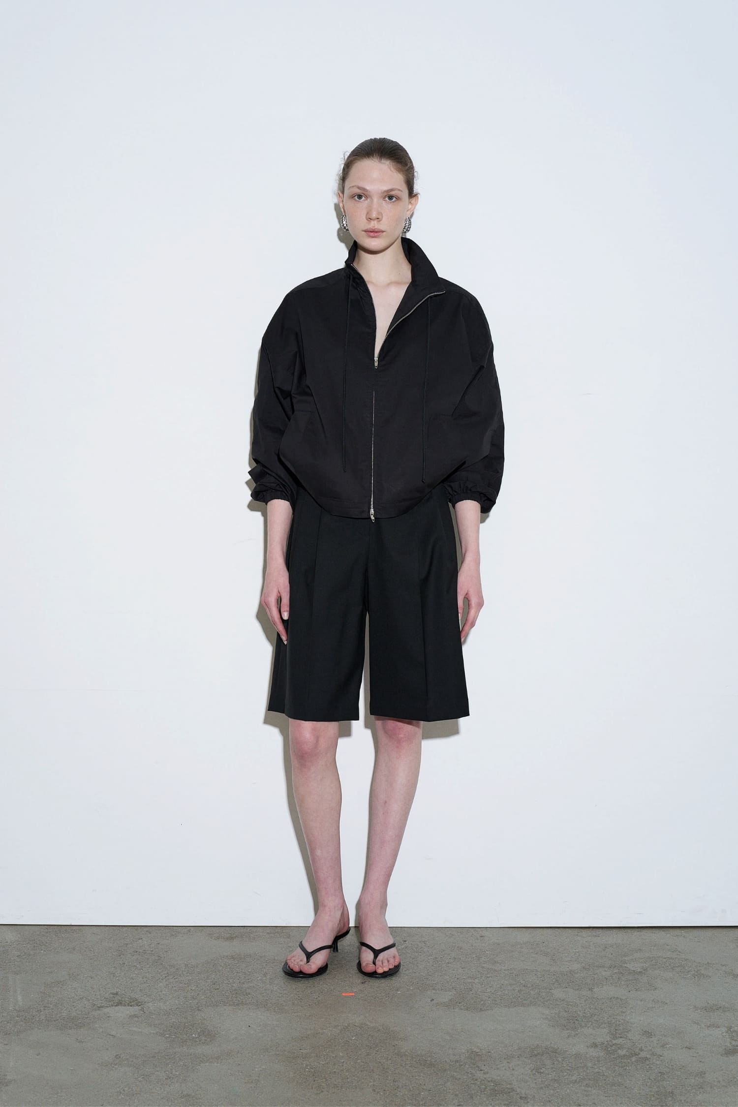 The Loom black drawstring neck jacket front view with relaxed fit and zip closure