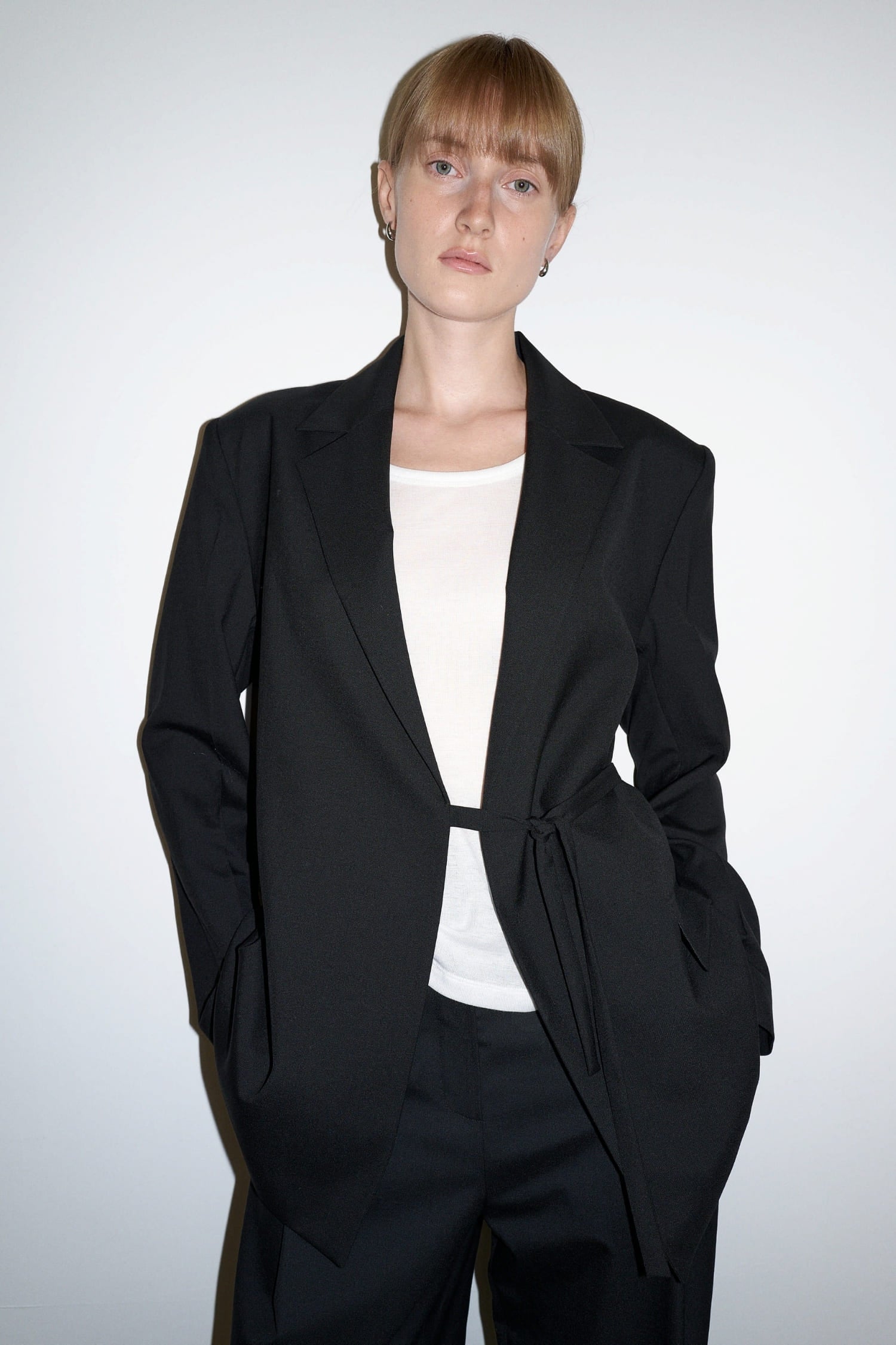  The Loom black wool jacket close-up showing notch lapel and side tie fastening detail | hover